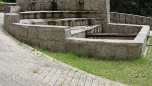 A stone structure with a series of steps and a central basin, surrounded by grass and trees. - Hostal Pablos House (Machu Picchu)