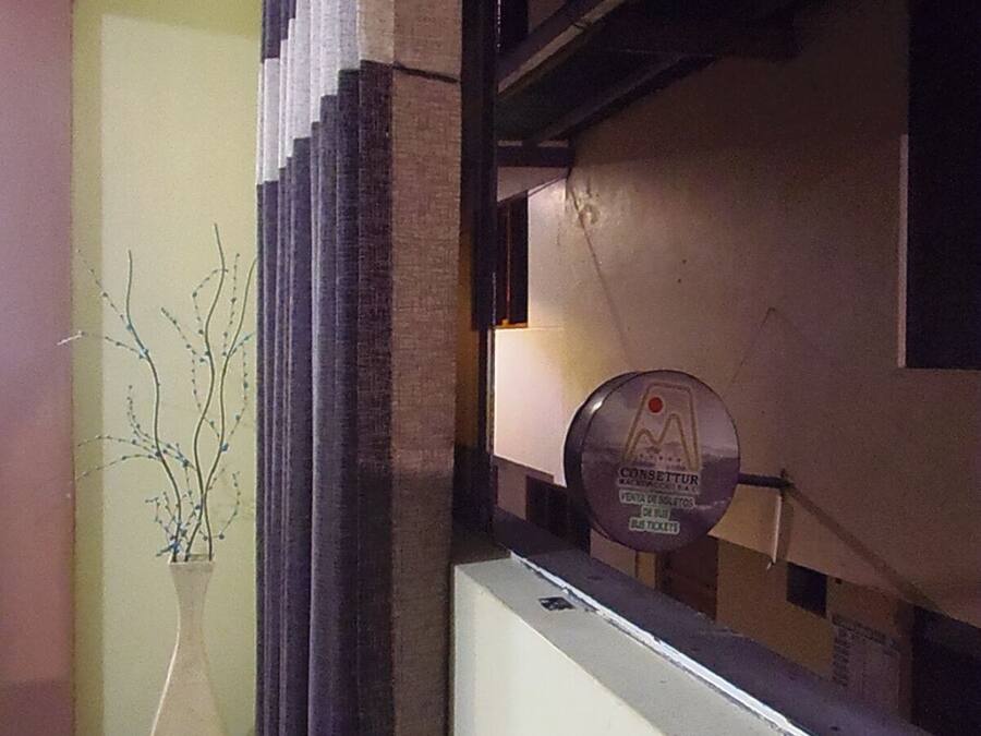 Un pasillo con un panel decorativo en la pared, un jarrón con ramas y un letrero redondo con texto.