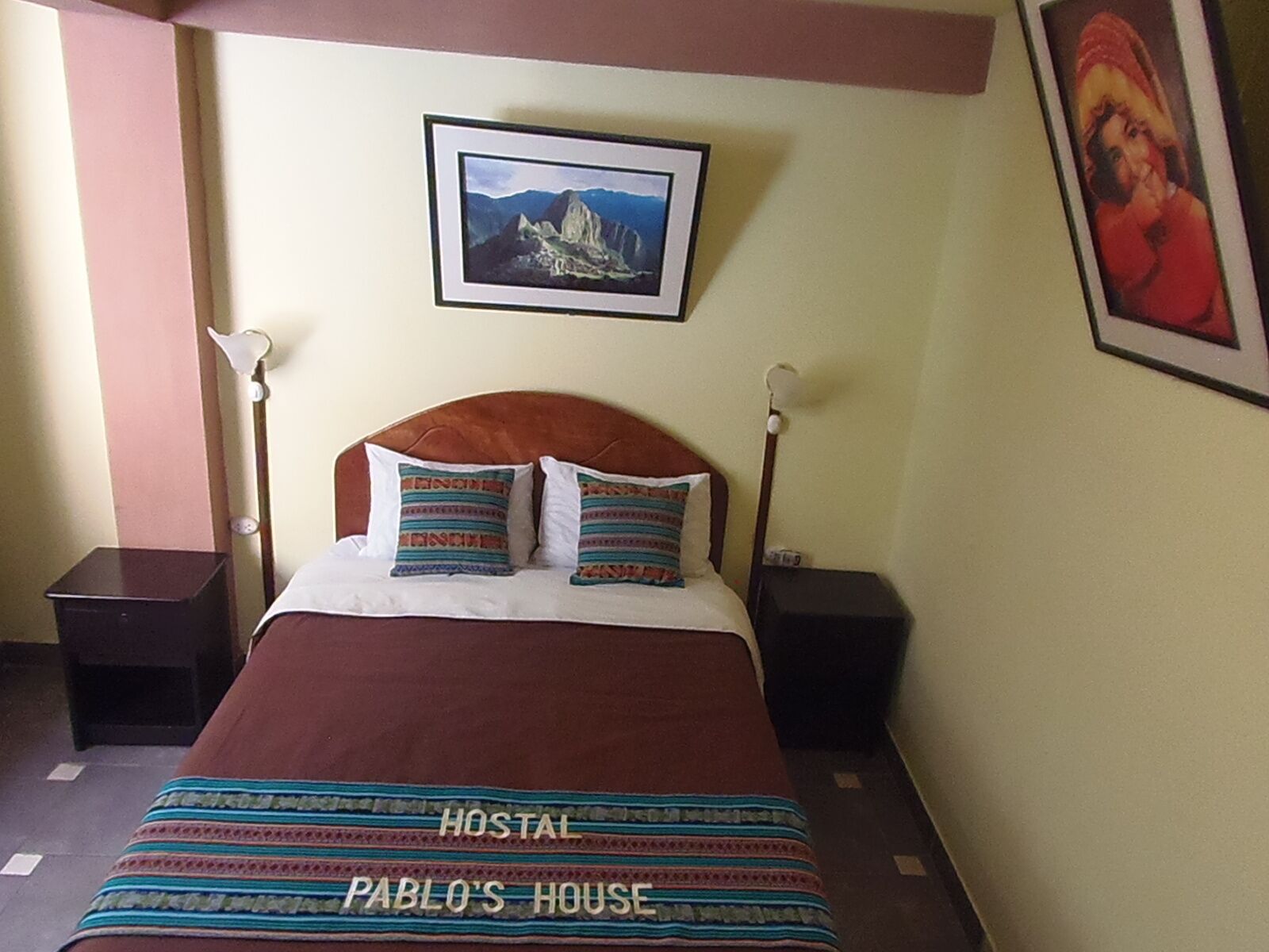 Una cama con cabecera marrón, dos mesitas de noche y un cuadro enmarcado sobre la cama.