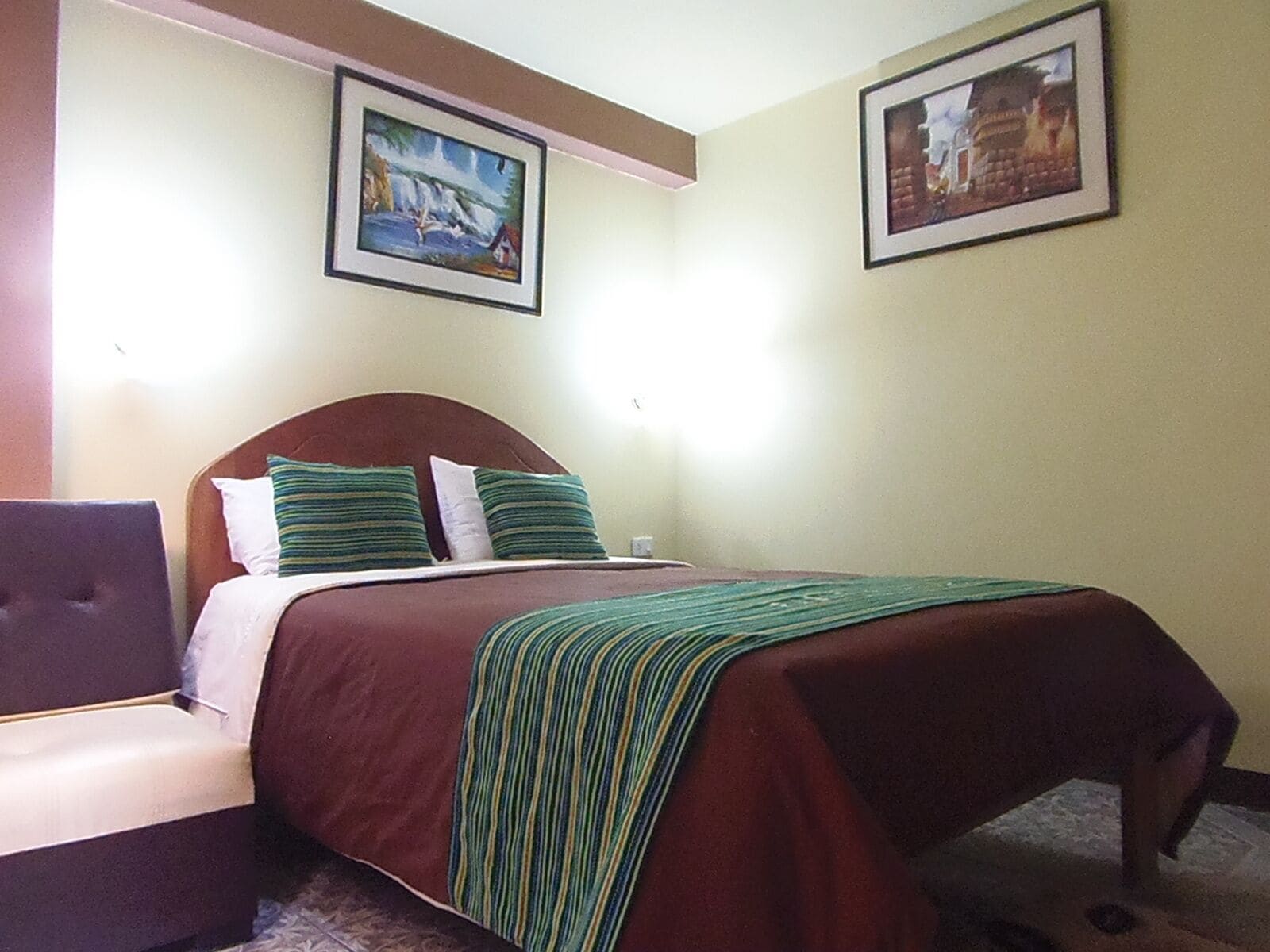 Una camera d'albergo con un letto, una sedia e due quadri appesi al muro.