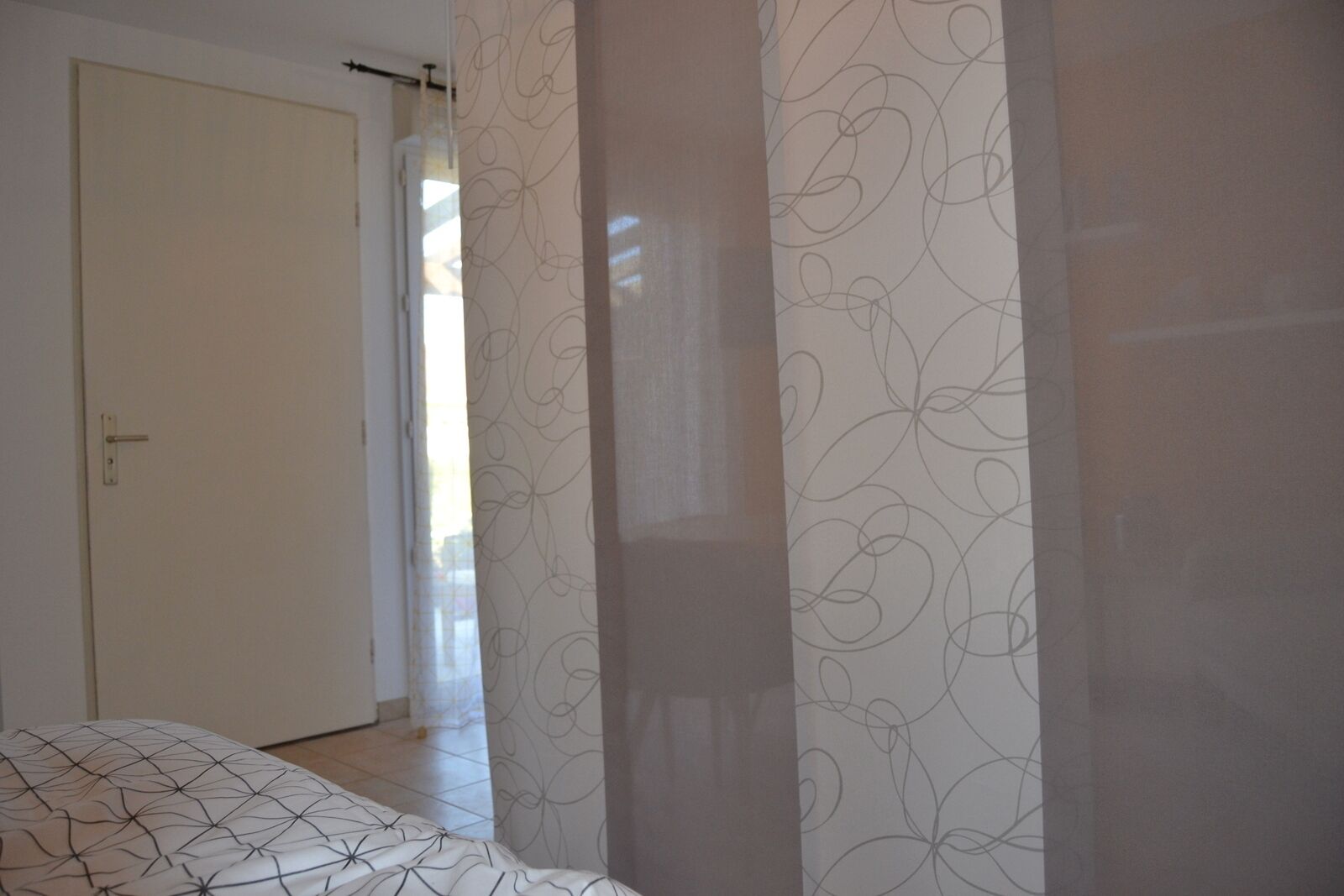 Une chambre à coucher avec un lit, une porte et un rideau orné d’un motif floral.