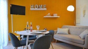 A modern living room with a sofa, dining table, chairs, a TV, and a wall-mounted shelf with a 'HOME' sign.