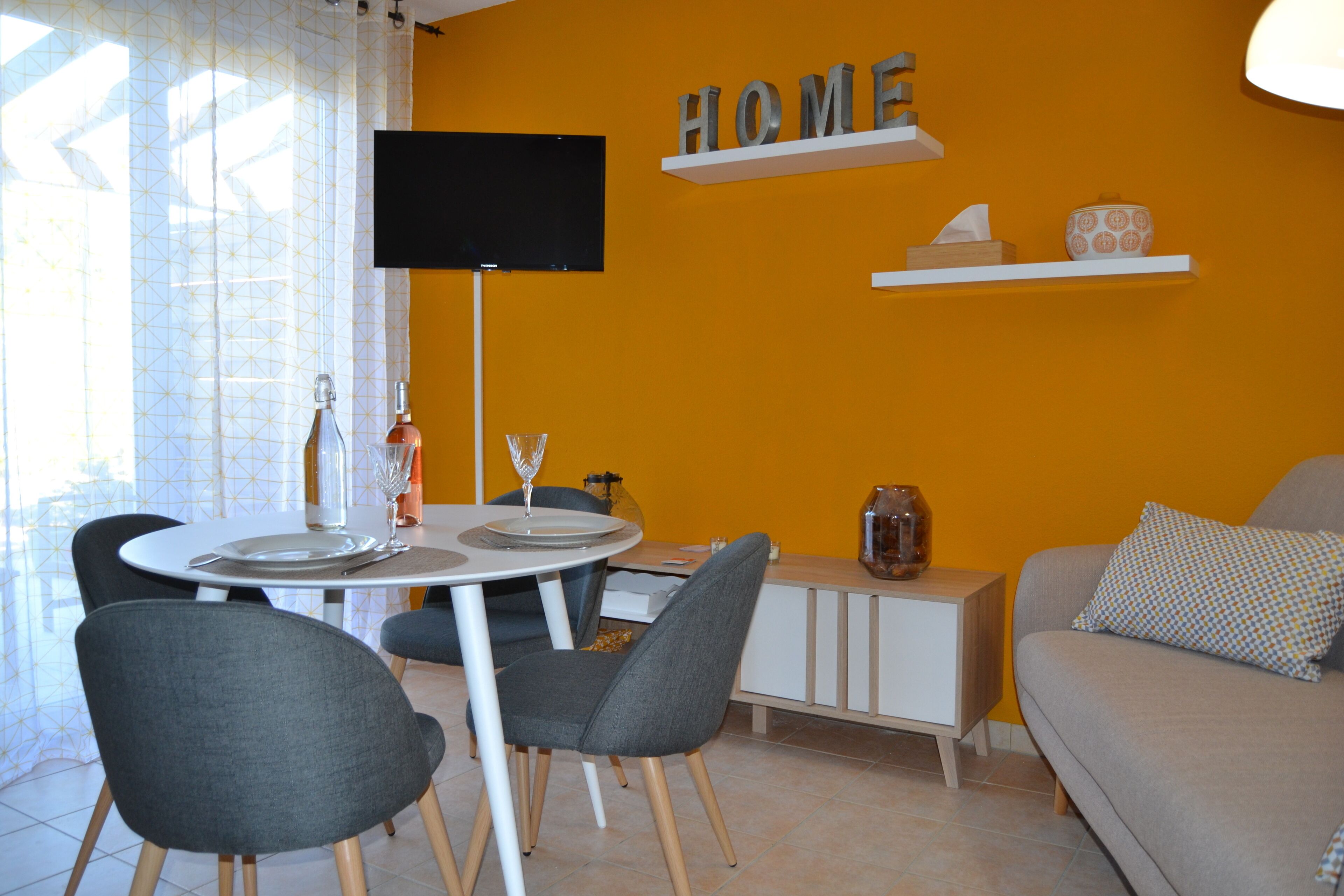 A dining area with a table set for two, a sofa, and a TV mounted on the wall.