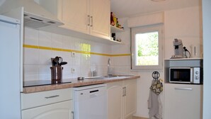 A compact kitchen with white cabinets, a dishwasher, a microwave, and a window providing natural light.