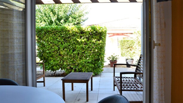 An outdoor patio area with a wooden table and chairs, a bench, and a large hedge.