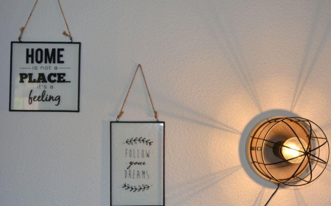 Twee aan de muur bevestigde borden met motiverende citaten en een moderne wandlamp met zichtbare gloeilamp.