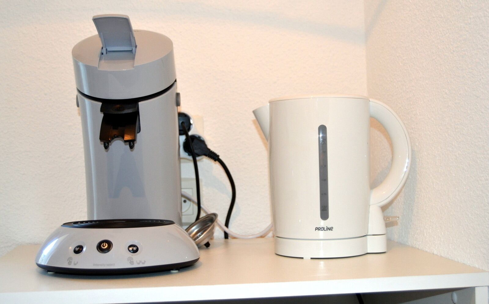 Une machine à café et une bouilloire sur un plan de travail blanc.