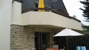 A house with a stone exterior, a balcony with a yellow umbrella, a table with chairs, and a blue-striped lounge chair. - Apartment with garden in quiet residence near beaches wi fi parking (Quiberon)
