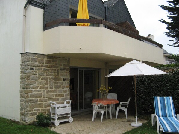 A house with a stone exterior, a balcony with a yellow umbrella, a table with chairs, and a blue-striped lounge chair.