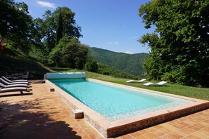A rectangular swimming pool with a tiled deck, surrounded by lush greenery and hills in the background. - Mas Soubiranne on the heights of Céret (Céret)