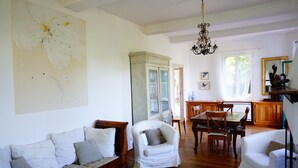 A spacious living room with a wooden floor, a white sofa, a white armchair, a dining table with chairs, and a large map on the wall. - Mas Soubiranne on the heights of Céret (Céret)