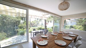 Een eethoek met een houten tafel gedekt voor vier personen, grote ramen met uitzicht op de tuin en omliggende huizen.