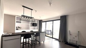 A modern kitchen with a bar area, white cabinetry, and a large sliding glass door leading to a balcony. - Luxury apartment for 4, beachfront, balcony, pool, pets allowed, parking, WiFi (La Tranche-sur-Mer)
