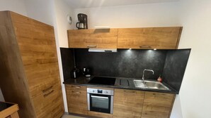 A compact kitchen with wooden cabinets, a black countertop, a built-in oven, a sink, and a coffee maker. - Spacious 3* Apartment - 6 ppl with balcony in Châtel (Châtel)