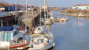 Un puerto deportivo con varias embarcaciones amarradas, un puente al fondo y edificios a lo largo de la orilla.