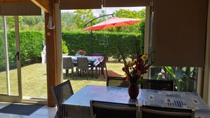 Un patio con mesa y sillas, un paraguas rojo y vistas a un jardín.