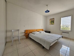 A bedroom with a bed, a chair, a nightstand, a window, and a ceiling fan.