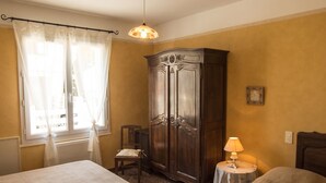 Ein Zimmer mit zwei Betten, einem Holzschrank, einem kleinen Tisch mit einer Lampe und einem Fenster mit Vorhängen.