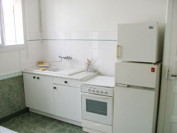 Een keuken met een spoelbak, fornuis en koelkast.