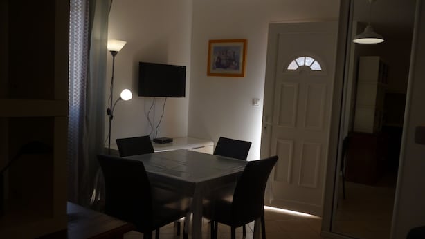 A dining area with a table and chairs, a TV mounted on the wall, and a door leading to another room. - studio in quiet and sunny property near the sea. (monticello)