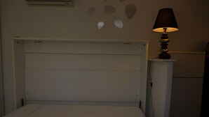 A bed with a headboard, a bedside table, a lamp, and a wall with decorative elements. - studio in quiet and sunny property near the sea. (monticello)