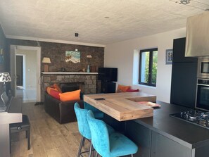Een moderne keuken met een stenen muur, een open haard, een eethoek met blauwe stoelen en een groot raam.