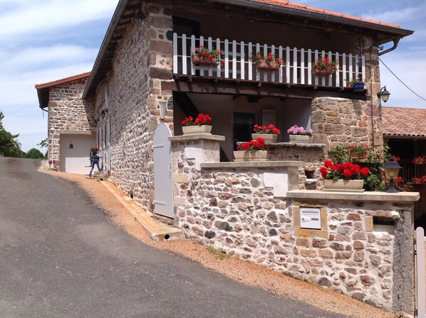 A stone building with a balcony, potted flowers, and a small entrance.