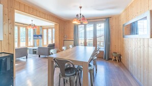 Ein Zimmer mit Holzwandverkleidung, einem großen Esstisch, mehreren Stühlen, einem Sofa und einem Fernseher.