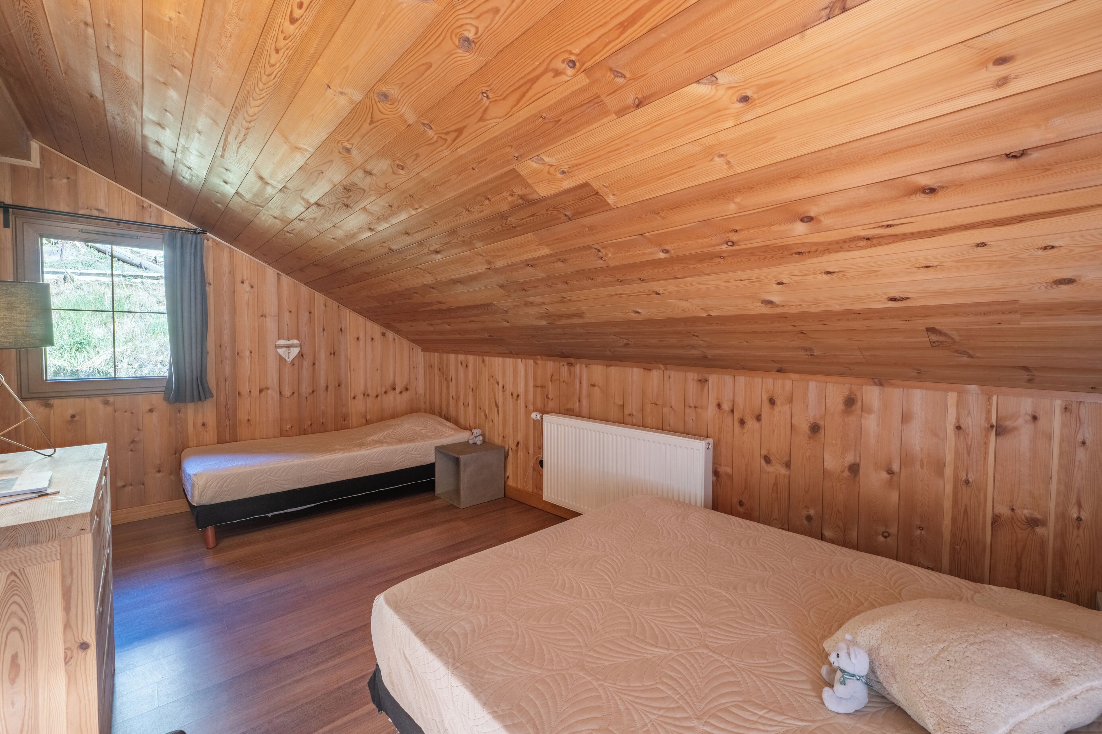 Une cabane en bois chaleureuse, dotée de deux lits simples, d’un bureau et d’une fenêtre avec des rideaux.