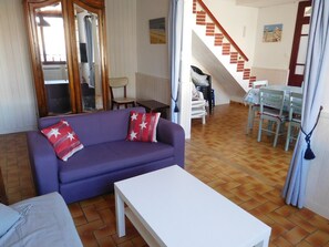 Cozy living space with a sofa, coffee table, and dining area, featuring a staircase leading to an upper level.