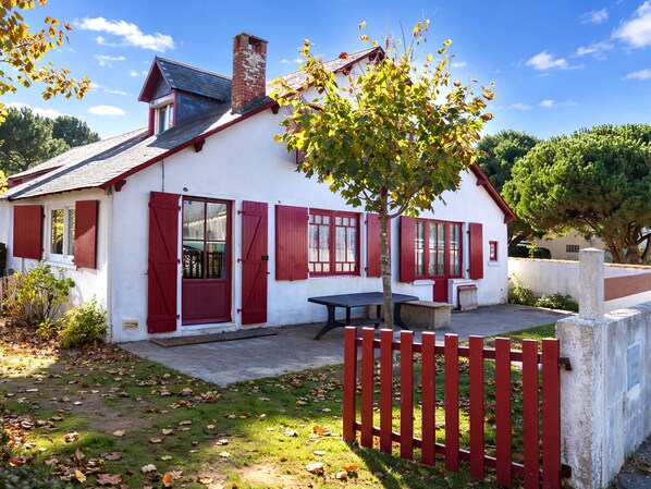 A white building with red shutters, a chimney, and a picnic table in the yard.