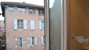 Vista de un edificio de ladrillo con varias ventanas y contraventanas, una puerta con picaporte blanco y un pequeño balcón.