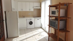 Una cocina funcional con refrigerador, lavadora, microondas y estante de madera.