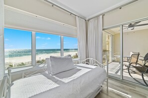 A bedroom with a large window overlooking a beach, a balcony with outdoor furniture, and a ceiling fan. - Come Enjoy this luxury condo right on the beach of Gulf Shores! (Orange Beach)