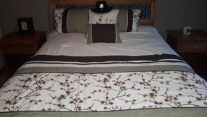 Un llit ben fet amb un llençol estampat amb motius florals, un capçal de fusta i un barret decoratiu al capçal.