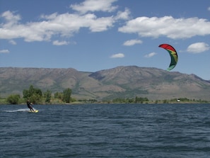 Eine Person windsurft auf einem See, im Hintergrund Berge.