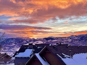 Un paisaje montañoso con tejados y casas cubiertas de nieve, bajo un cielo de atardecer colorido.
