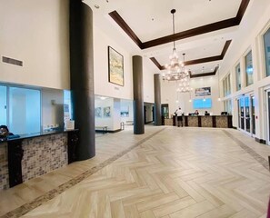 Un hall d’entrée spacieux, doté d’un sol en parquet à motifs en chevrons, de grandes colonnes, d’un comptoir d’accueil et d’un lustre moderne.
