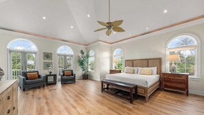 Un dormitorio amplio con una cama grande, ventilador de techo y varias ventanas.