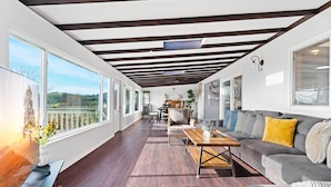 Un salón amplio con piso de madera, un sofá gris, una mesa de centro de madera y vistas a un lago a través de ventanas grandes.