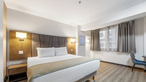 Habitación de hotel con cama, lámparas de noche, escritorio y ventana con cortinas.