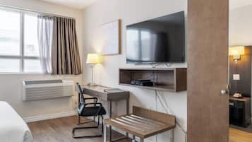 Una habitación de hotel con escritorio, silla, televisión, aire acondicionado y cama.