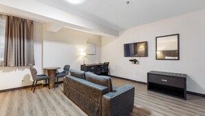 Una habitación de hotel moderna con sofá, sillas, escritorio, televisor y televisor de pantalla plana en la pared.