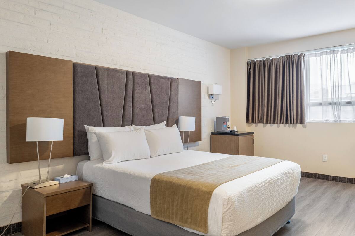 Hotelkamer met een groot bed, twee nachtkastjes, een wandlamp, een raam met gordijnen en een metselwerkmuur.