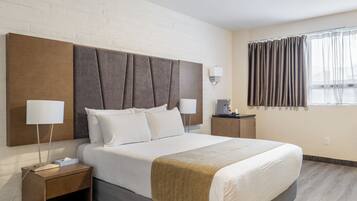 Una habitación de hotel con una cama grande, dos mesitas de noche, una lámpara de pared, una ventana con cortinas y una pared con diseño de ladrillo.