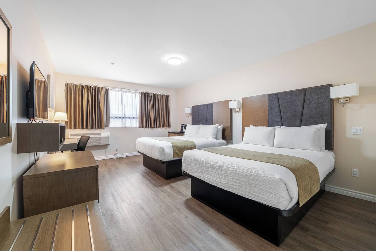 Een hotelkamer met twee bedden, een bureau, een stoel, een televisie en een raam met gordijnen.