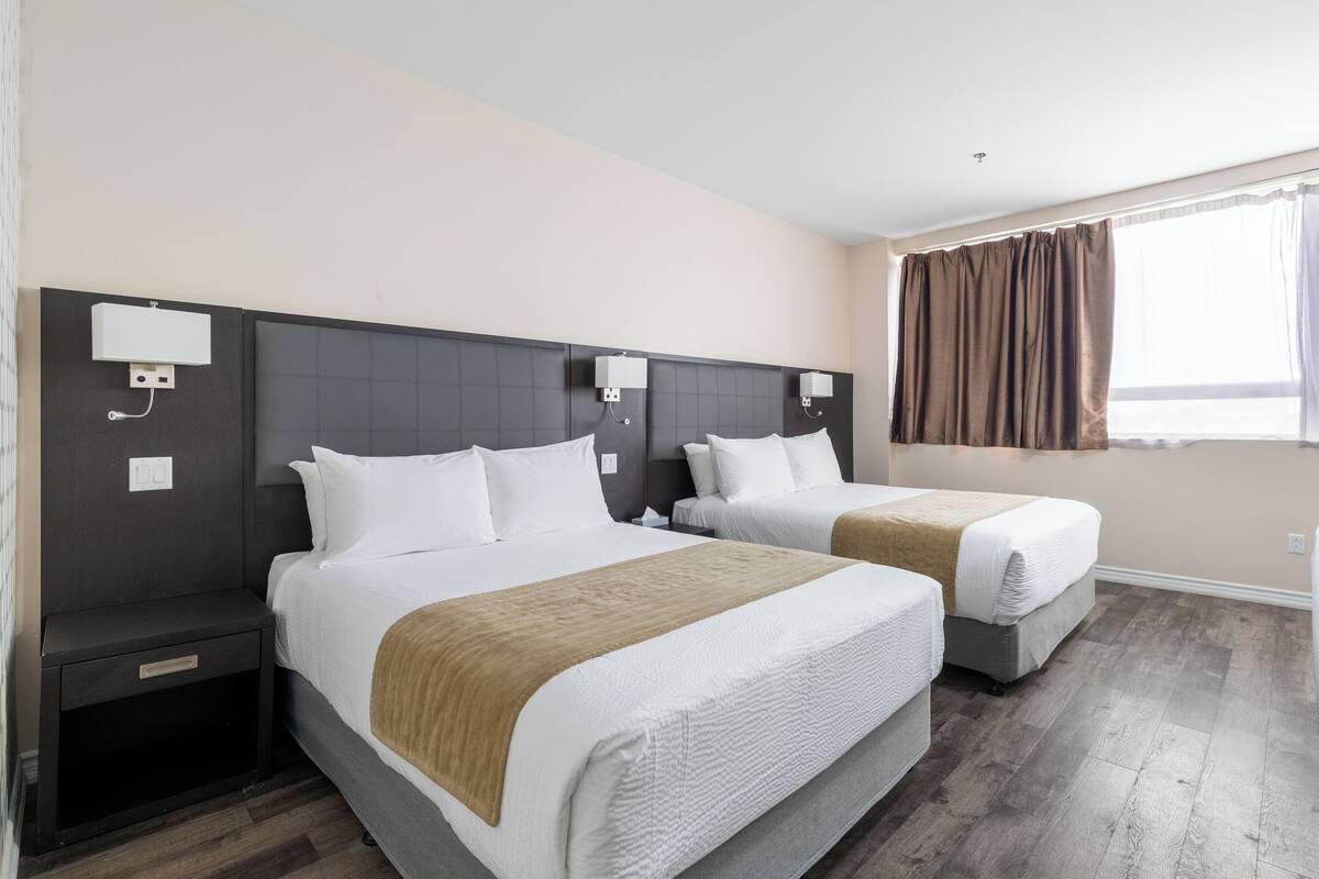 Een hotelkamer met twee bedden, een donker hoofdeinde, een raam met gordijnen en een houten vloer.
