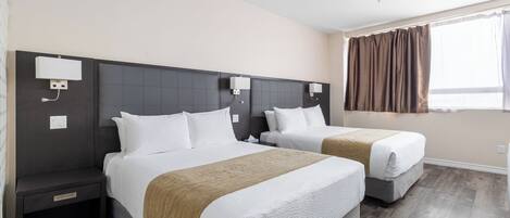 A hotel room with two beds, a dark headboard, a window with curtains, and a wooden floor.