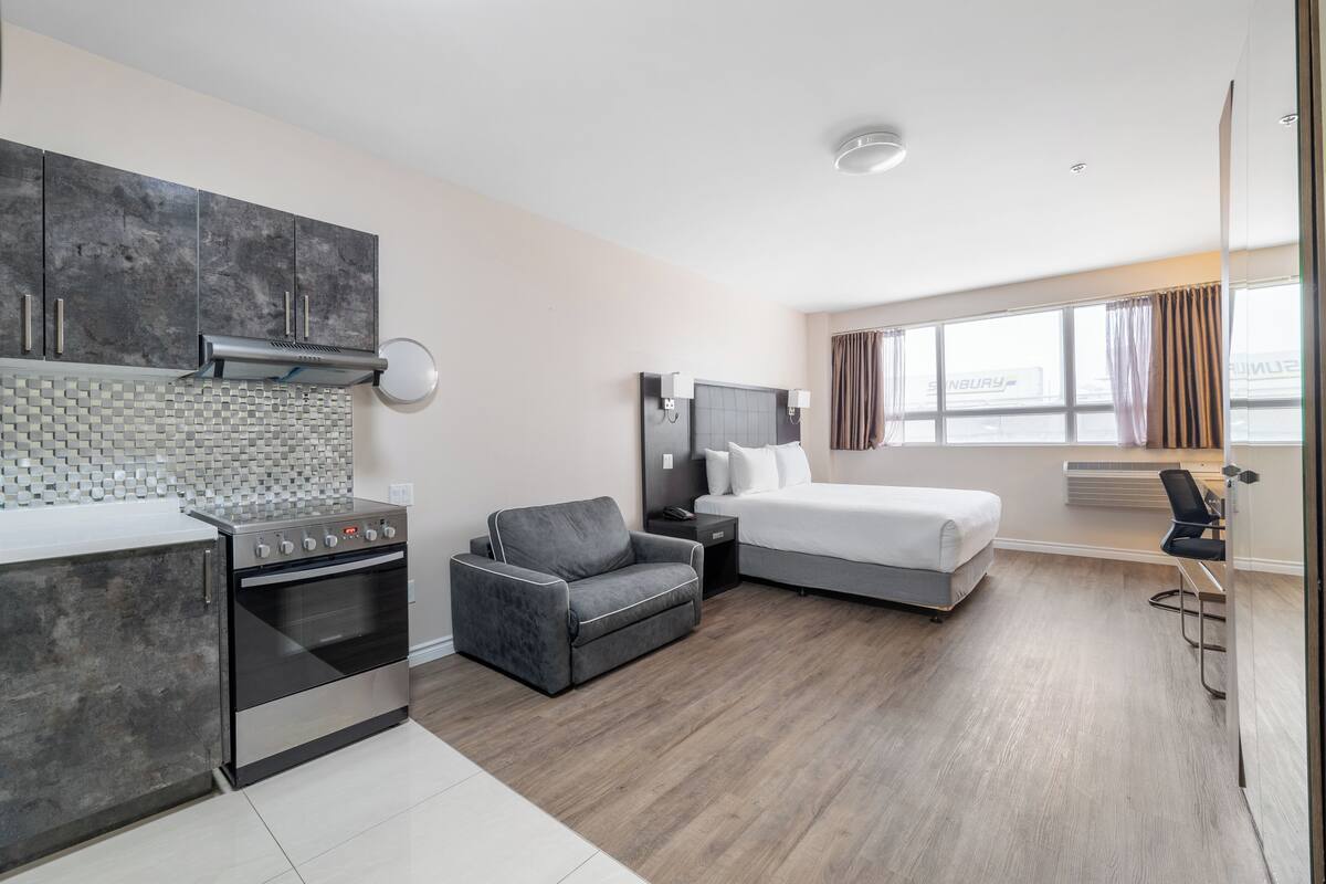 Een moderne hotelkamer met kitchenette, een bed, een slaapbank en een groot raam.