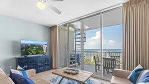 Una sala de estar con televisor, sofá, mesa de centro y un balcón con vistas al mar.